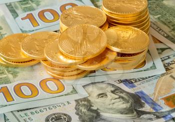 Stack of golden eagle coins on new design of US currency one hundred dollar bills with Benjamin Franklin portrait