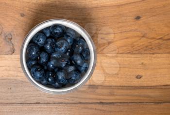 Aerial or top view of a white glass bowl of organic blueberries freshly washed and sitting on old wood table surface