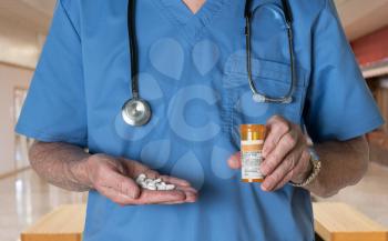 Senior male doctor with stethoscope in medical scrubs and holding bottle and tablets of Oxycodone to illustrate opioid epidemic