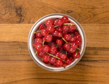 Aerial or top view of a white glass bowl of organic redcurrant or red currant fruit  sitting on old wood table surface