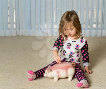 Young girl on floor of home saving money in a piggy bank for expenses in the future