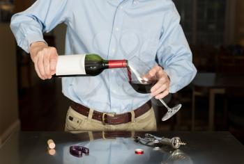 Senior caucasian man standing in kitchen pouring from bottle of red wine with a blank label for copy space