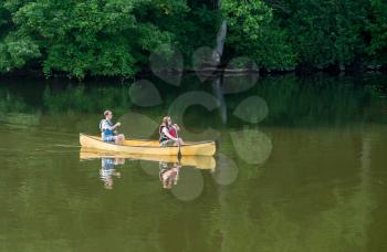 Male and female caucasian couple paddling a yellow canoe on a very calm morning on tree lined lake