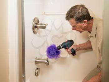 Senior working man cleaning a shower or bath with a power drill