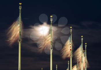 US Flags flutter in front of moon by Washington Monument on a clear night in Washington DC, United States of America