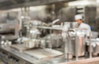 Defocused chef preparing food in commercial stainless steel kitchen in restaurant