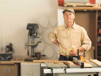 Senior man working on tools in home workshop with table saw, bench drill and other equipment