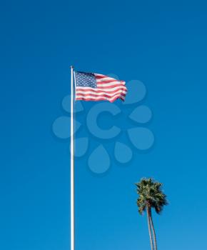 Wind blows the USA flag against blue sky alongside palm tree at the memorial at recreation point in Laguna Beach