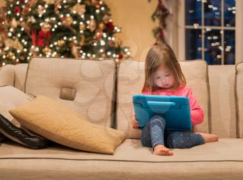Young girl sitting at home on settee and using a child's tablet touch screen computer at xmas suggesting this was a present