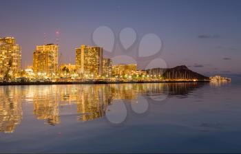 Panorama of the nightime skyline of Honolulu and Waikiki from Ala Moana park after the sun sets with artificial water reflection