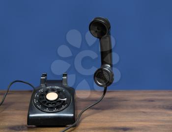 Old and antique rotary telephone on wooden desk with handset floating in the air ready for call