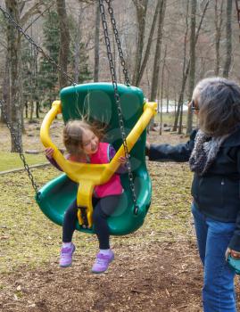 Grandma with her young granddaughter playing in a modern plastic swing in forest playground
