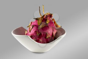 Dragon fruit with distinctive red skin in a white pottery bowl against a grey background