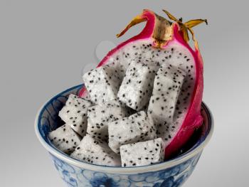 Dragon fruit cut in half with distinctive red skin in a blue pottery bowl against a grey background