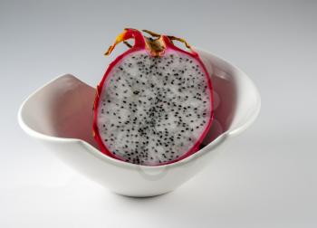 Dragon fruit cut in half with distinctive red skin in a white pottery bowl against a grey background