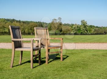Teak chairs in a large expansive garden with trees in background