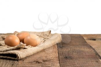Easter background with brown organic eggs arranged on burlap sack on rustic wooden table with isolated background