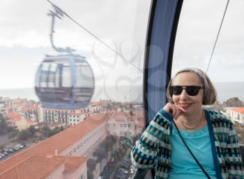Smiling female tourist in cable car over the city of Funchal in Madiera