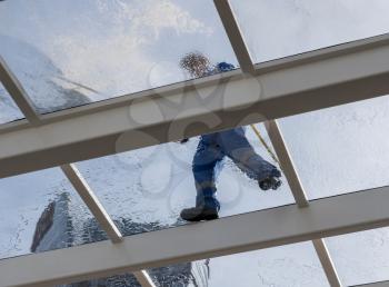 Male worker washing large expanse of glass roof over swimming pool with hose pipe