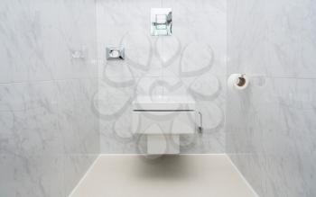Wall mounted minimalist toilet or WC in luxury tiled bathroom with push button flush