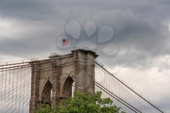 Abstract details of the suspension cables at the top of the Brooklyn Bridge structure with US Flag against stormy sky