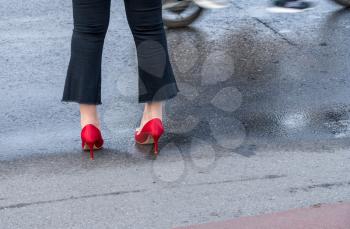 Woman wearing flared denim jeans and red high heeled shoes waits by roadside in China