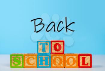 Stack of wooden blocks stacked to spell Back to School against blue background with copy space