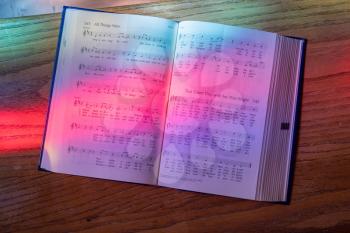 Colored light from stained glass window in methodist church falls across open hymnal for Easter hymn