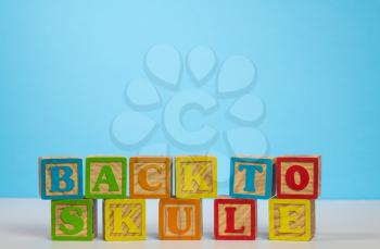 Stack of wooden blocks wrongly spelling Back to School as Skule against blue background with copy space