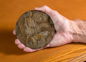 Hand holding historic memorial plaque or remembrance medal created in 1917 for British Soldiers who died in the Great War