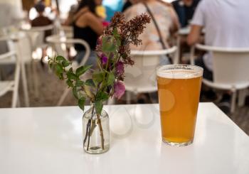 Focus on a cold glass of IPA beer with decorative flowers on white table in Lisbon bistro
