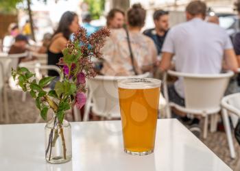 Focus on a cold glass of IPA beer with decorative flowers on white table in Lisbon bistro