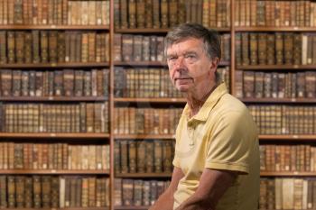 Senior old man looking at camera with a background of shelves of old books as if in library of a stately home