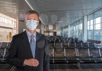 Senior adult executive wearing suit and face mask to travel through airport due to coronavirus