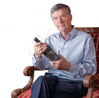 Friendly senior retired man examining a wine bottle label while seated in chair and isolated or cutout against a white background