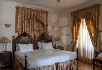 Double bed in traditional luxury hotel room with drapes and wooden floor