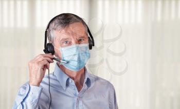 Senior caucasian man wearing facemask using headset to talk to customers or team during coronavirus epidemic