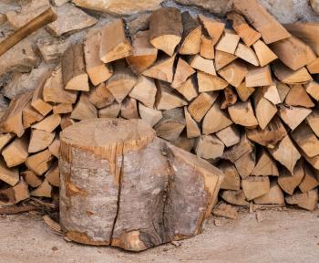 Chopped wood and axe stacked against the stone wall of a rustic farmhouse
