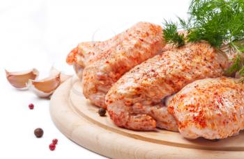 Spicy raw chicken wings on a wooden  board with dill and garlic