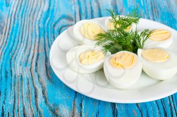Boiled hen eggs and green dill in a white plate on a blue wooden background