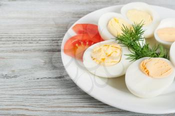 Boiled hen eggs and tomato in a white plate on a wooden background