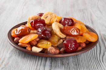 Dried fruits on a wooden background. Dates, lemon, apricots, figs and nuts in a clay plate. 