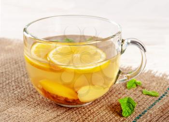 Glass cup of hot ginger tea with peppermint and lemon