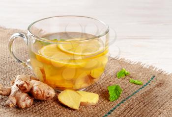 Glass cup of hot ginger tea with lemon and peppermint. Winter herbal drinks concept