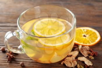 Glass cup of hot ginger tea with lemon, spices and peppermint on a wooden background. Winter hot herbal drinks concept