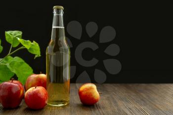Hard apple cider in a glass bottle, red ripe apples and green leaves on a black background