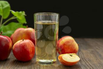 Hard apple cider in a glass, red ripe apples and green leaves on a black background