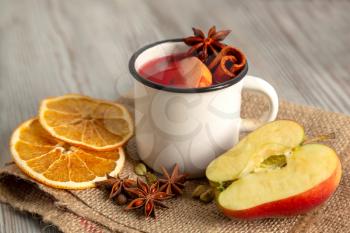 Mulled wine in white mug with fruit and spices on a wooden background. Traditional Christmas hot drink with red wine, apples, oranges, anise and cinnamon.
