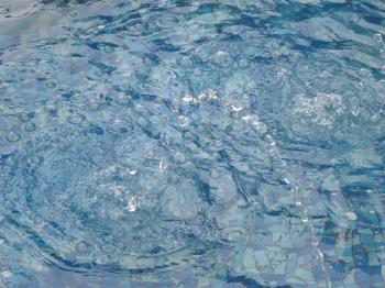 Waves from drops on a blue water of swimming pool