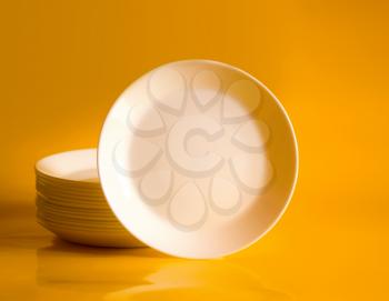 A few white, clean, empty plates on a bright yellow background